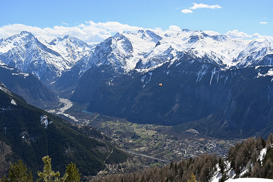 Photo d'ambiance uniquement : vue plongeante sur la plaine du Bourg-d'Oisans depuis le Signal de Villard (avril 2026), sommets enneigés, parapente dans le ciel 